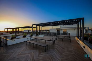 Rooftop deck entertainment area  and a pergola is set against a sunset sky.